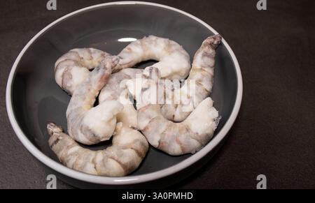 Gamberetti di tigre crudi congelati in una ciotola grigia su un tavolo da cucina grigio Foto Stock
