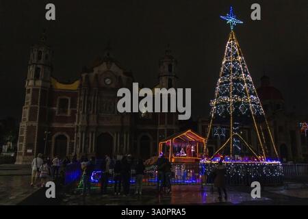 Un albero di Natale splendidamente decorato e un presepe illuminano di fronte alla storica Basilica di Guadalupe, attirando i visitatori di notte. Foto Stock