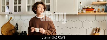 Un giovane dall'aspetto gradevole con capelli ricci si trova nella sua elegante cucina per assaporare caffè e striscioni Foto Stock