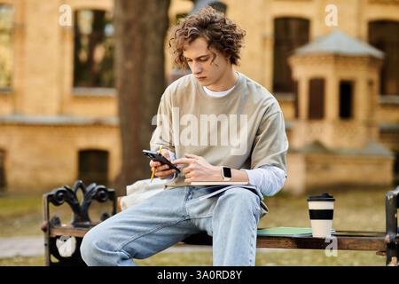 Un giovane uomo elegante seduto comodamente all'aperto, avvolto nel suo smartphone. Foto Stock