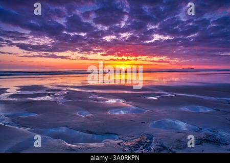 Una vista all'alba in estate dalla spiaggia di Bamburgh nel Northumberland guardando verso le isole fate con una graziosa e colorata formazione di nuvole Foto Stock