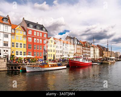 Vivace canale Nyhavn con case storiche colorate, barche ormeggiate e turisti che passeggiano lungo la banchina a Copenaghen, Danimarca Foto Stock