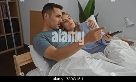 Coppia che si rilassa a letto, uomo e donna si coccolano insieme in una camera accogliente, godendosi la compagnia reciproca e guardando la tv, creando un ambiente caldo e intimo Foto Stock