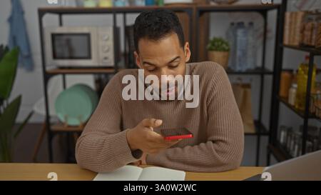 Giovane in ufficio che utilizza lo smartphone mentre lavora da casa circondato da libri e gadget, con un ambiente di lavoro moderno e dinamico wi Foto Stock