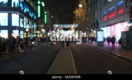 Vista sfocata della affollata strada di londra di notte con luci bokeh che catturano la vivace atmosfera invernale, con persone che passeggiano lungo l'illumin Foto Stock