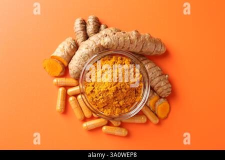 Polvere di curcuma in ciotola, radici e capsule su fondo arancione, in posizione piatta Foto Stock