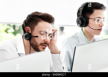 Un rappresentante del call center stanco e i suoi colleghi al lavoro ufficio open space Foto Stock