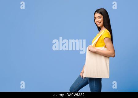 Giovane donna Asiatica con una borsa da shopping in tela di Tote vuota in posa Su sfondo viola Foto Stock