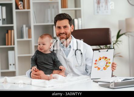 Seduti e sorridenti. Il medico con un bambino piccolo sta lavorando nell'armadietto. Foto Stock
