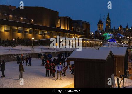 Ottawa, Canada - 8 febbraio 2025: Persone che pattinano sul Rideau Canal sotto il ponte in inverno. In centro di sera Foto Stock