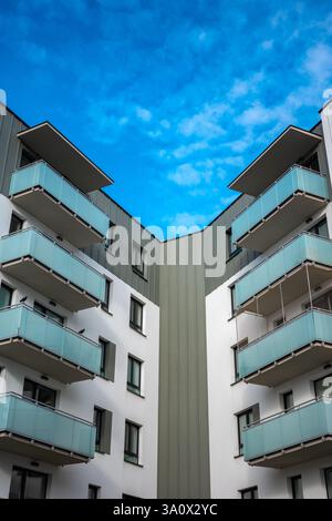 La facciata di un moderno edificio di appartamenti di colore grigio chiaro si affaccia sul cielo blu. Gli appartamenti sono dotati di balconi smaltati. Foto Stock