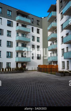 La facciata di un moderno edificio di appartamenti di colore grigio chiaro si affaccia sul cielo blu. Gli appartamenti sono dotati di balconi smaltati. Foto Stock