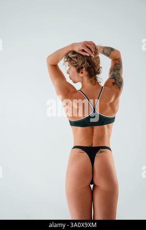 Tatuaggi sulla mano e sul retro. Giovane donna caucasica con forma fisica atletica è al chiuso di giorno. Foto Stock