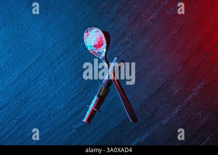 Tossicodipendenza. Cucchiaio con polvere e siringa su un tavolo con texture scura con luci al neon, in posizione piatta Foto Stock