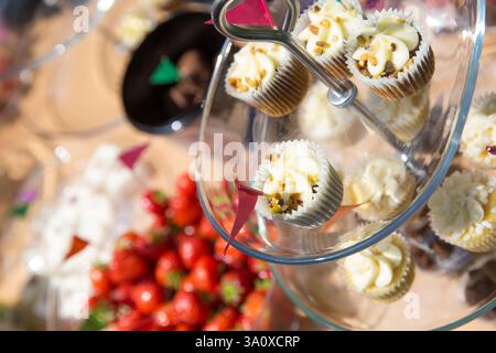 Cupcake, probabilmente a una festa, esposti su un banco di vetro a più piani con fragole. Forse ad un evento della comunità. Foto Stock