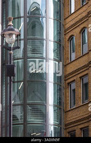 Moderno edificio in vetro con una facciata curva che riflette un vecchio edificio in mattoni. Contrasto negli stili architettonici. Foto Stock