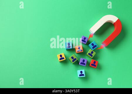 Magnete che attrae cubi colorati con figure umane su sfondo verde, vista dall'alto. Reclutamento o acquisizione di clienti Foto Stock