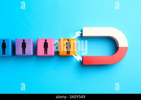 Magnete che attrae cubi colorati con figure umane su sfondo azzurro, vista dall'alto. Reclutamento o acquisizione di clienti Foto Stock