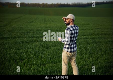 Camminare, tenere in mano il blocco note. Bel giovane uomo è in campo agricolo. Foto Stock