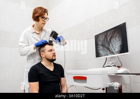Un dermatologo esamina e analizza la pelle di un giovane paziente in una clinica moderna utilizzando attrezzature avanzate. Foto Stock