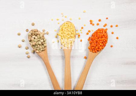 Lenticchie rosse, verdi e gialle in cucchiaio di legno e ciotola su fondo rustico bianco, legumi di lenticchie secche crude Foto Stock