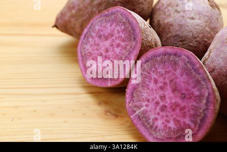 Primo piano di sezione trasversale di patate dolci viola crude con radici intere sfocate sullo sfondo Foto Stock