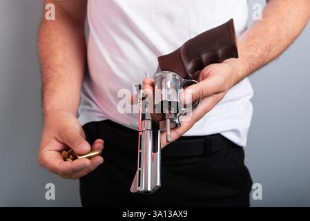 Dettaglio delle mani di un istruttore di tiro che tiene una pistola in una mano e dei proiettili nell'altra mano. Isolato su sfondo grigio. Pratica sportiva. Foto Stock
