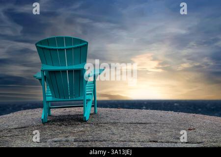 Sedia Adirondack vuota, su un grande masso, che guarda il tramonto all'orizzonte Foto Stock