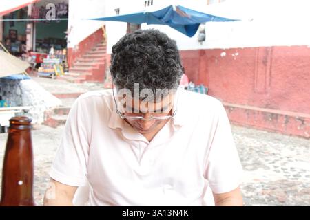 Un uomo messicano seduto con i capelli ricci che guarda per terra. Foto Stock