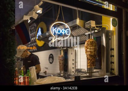 Mosca, Russia - 12 settembre 2024. Insegna al neon di un caffè su un chiosco shawarma. Uno chef maschile prepara lo shawarma, affettando la carne nella pita. Foto Stock