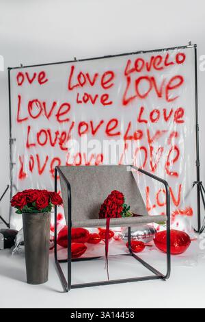 sedia in metallo con tessuto grigio e rose rosse con iscrizioni d'amore. area fotografica per san valentino Foto Stock