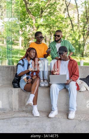 Gli amici studenteschi di colore lavorano su un notebook alla panchina del parco, chiacchierano sui social media, scrivono blog Foto Stock