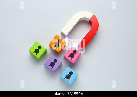 Magnete che attrae cubi colorati con figure umane su sfondo grigio chiaro. Reclutamento o acquisizione di clienti Foto Stock