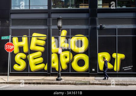 Boston, Massachusetts, Stati Uniti - 12 febbraio 2025 - Un uomo che cammina su un marciapiede tra le finestre degli edifici con il cartello giallo brillante Hello Seaport a Boston, Massachusetts Foto Stock