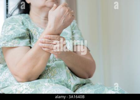 Donna asiatica matura che soffre di dolore in mano a casa, spazio per il testo. Sintomo reumatico. Messa a fuoco selettiva. Foto Stock