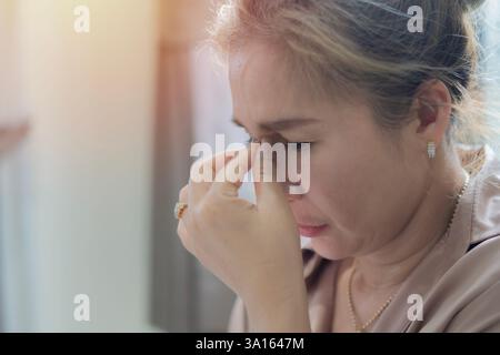 Matura pensiva triste donna di etnia asiatica anni '40 che indossa camicia marrone tenere gli occhi chiusi strofinare mettere mano sul naso. Copia spazio, messa a fuoco selettiva Foto Stock