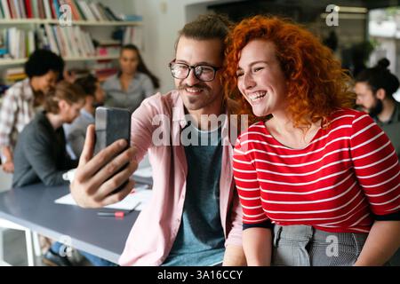 Amichevole felice collaboratore multietnico maschio e femmina divertirsi con lo smartphone, lavorando insieme Foto Stock