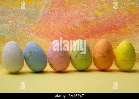 Sei uova di pasqua colorate sono disposte in fila. Le uova sono bianche, blu, rosa, verdi, arancioni e gialle. Foto Stock