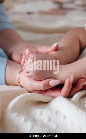 Una madre tiene delicatamente i piedi delicati del suo bambino, simboleggiando l'amore, la cura e il legame della maternità. Foto Stock
