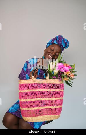 Donna nera sorridente che tiene in mano una borsa della spesa colorata e fiori Foto Stock