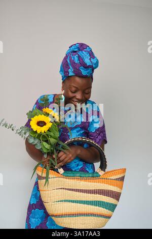 Donna che tiene in mano girasoli e una colorata borsa fatta a mano sorridente Foto Stock