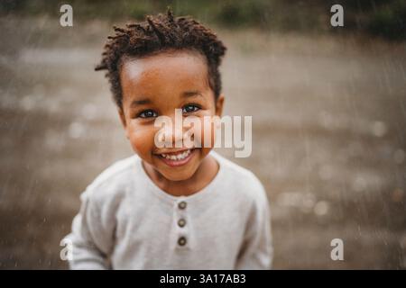 Ragazzo nero sorridente ballando sotto la pioggia in campagna Foto Stock