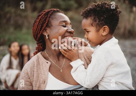 Sorridente mix race boy seduto sulla pancia della mamma incinta nera sorridente Foto Stock
