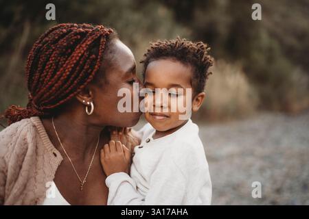Sorridente mix race boy seduto sul bacio della pancia della mamma incinta nera Foto Stock
