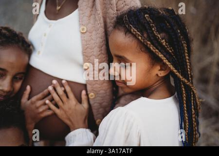 Madre incinta nera e figlie di razza mista che toccano la pancia Foto Stock