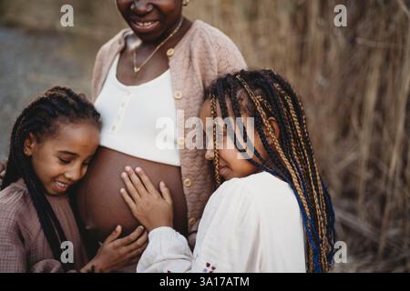 Madre incinta nera e figlie di razza mista che toccano la pancia Foto Stock