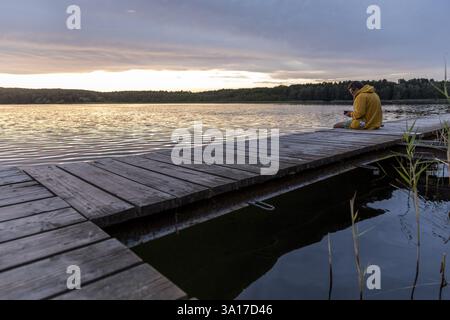 Uomo seduto sul molo del bagno e guardando il suo telefono cellulare, atmosfera serale al Grosser Glubigsee vicino a Wendisch Rietz, quartiere Oder-Spree, Bran Foto Stock