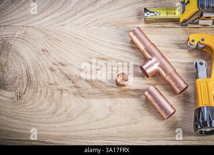 Connettori per tagliatubi per acqua in rame linea nastro su tavola in legno concetto di brassware per tubazioni per spazi di copia Foto Stock