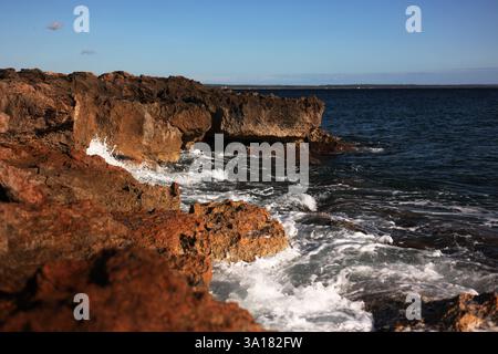 costa rocciosa con pietre rosse onde che si infrangono sulle rocce e spruzzi che volano. Foto Stock