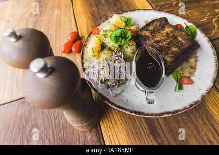 Primo piano di un saporito piatto fatto in casa con carne alla griglia, verdure vivaci e patate bollite condite, splendidamente placcate su un rustico tavolo in legno in un ambiente accogliente e invitante. Foto Stock
